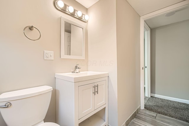 bathroom with wood finished floors, vanity, toilet, and baseboards