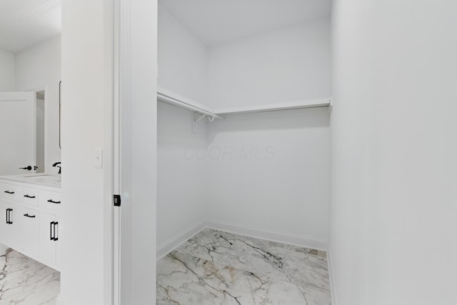 walk in closet with light marble finish floors and a sink