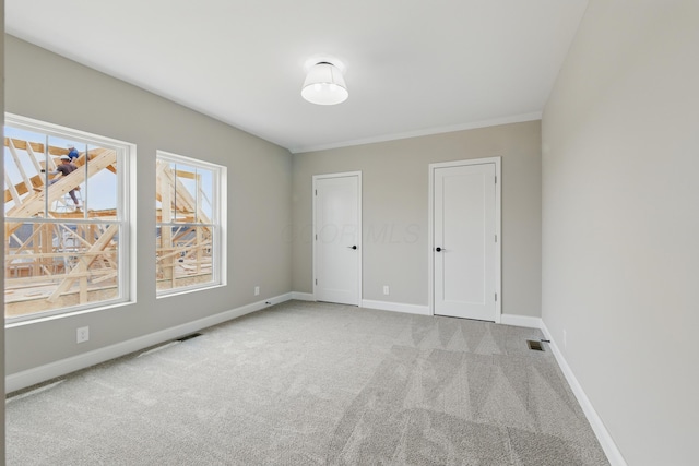 carpeted spare room featuring baseboards and crown molding