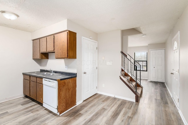 kitchen featuring white dishwasher, light wood-type flooring, a textured ceiling, brown cabinets, and a sink