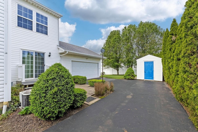 garage featuring central air condition unit, asphalt driveway, and a storage shed