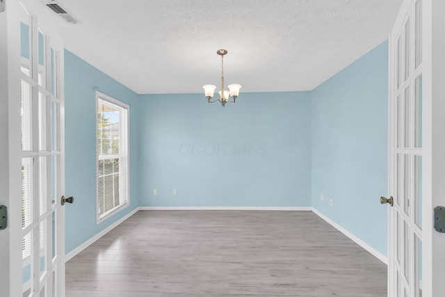 empty room featuring french doors, wood finished floors, a chandelier, baseboards, and a textured ceiling