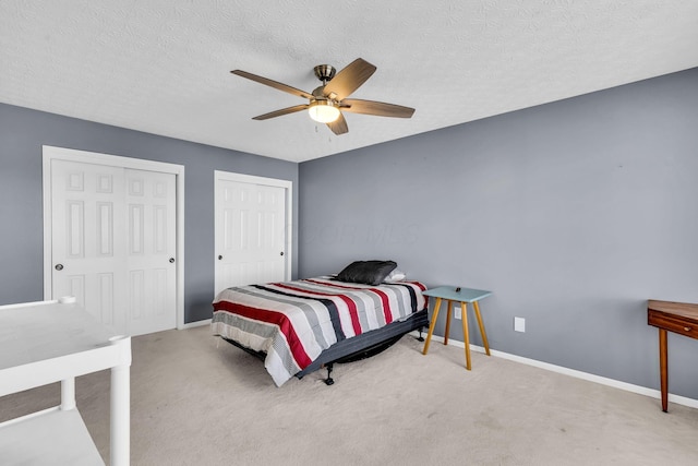 carpeted bedroom featuring two closets, baseboards, ceiling fan, and a textured ceiling