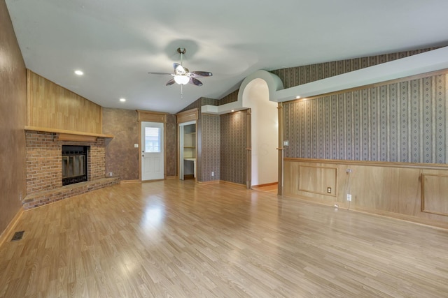unfurnished living room with a ceiling fan, light wood finished floors, a brick fireplace, lofted ceiling, and baseboards