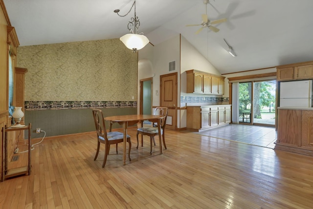 dining area featuring wallpapered walls, a wainscoted wall, ceiling fan, light wood-style floors, and high vaulted ceiling