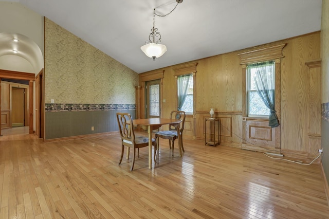 dining room featuring a wainscoted wall, light wood-type flooring, wallpapered walls, and vaulted ceiling