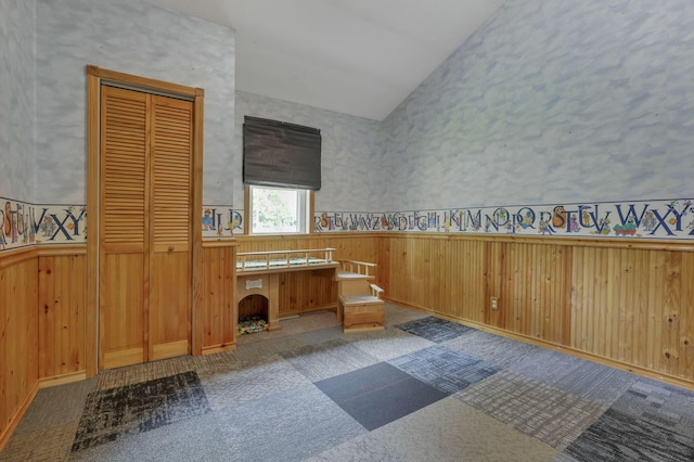 unfurnished bedroom with a wainscoted wall, lofted ceiling, and wooden walls