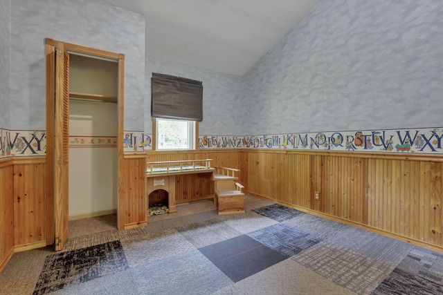 unfurnished bedroom featuring lofted ceiling, wainscoting, and carpet