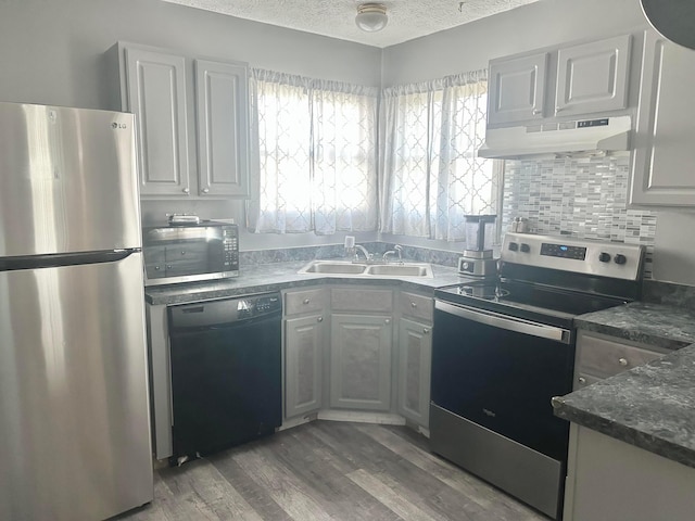 kitchen featuring appliances with stainless steel finishes, under cabinet range hood, a sink, a textured ceiling, and dark countertops