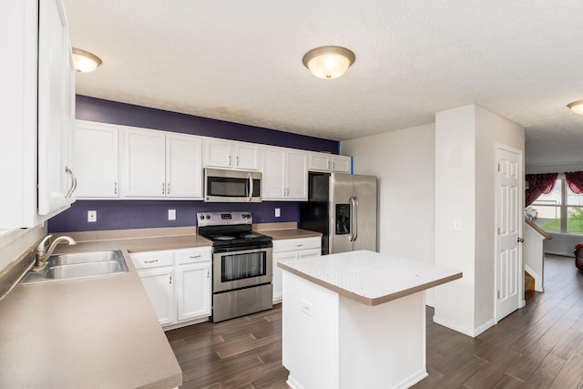kitchen featuring appliances with stainless steel finishes, a sink, dark wood-type flooring, white cabinetry, and light countertops