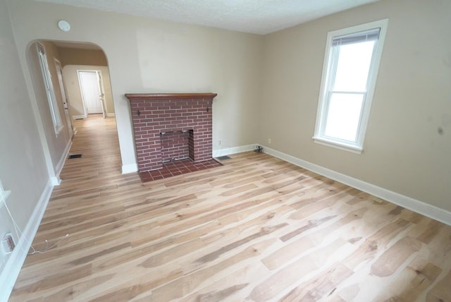 723 N Maple St, Lancaster, OH 43130 - unfurnished living room featuring light wood finished floors, arched walkways, baseboards, a brick fireplace, and a textured ceiling