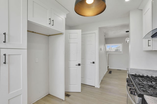 841 Saint Clair Ave, Columbus, OH 43201 - kitchen with stainless steel range with gas cooktop, white cabinets, light wood-style floors, light stone counters, and wall chimney exhaust hood
