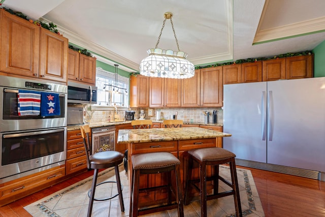 7563 Jenkins Dr, Canal Winchester, OH 43110 - kitchen with appliances with stainless steel finishes, a kitchen island, decorative backsplash, light wood-style flooring, and crown molding