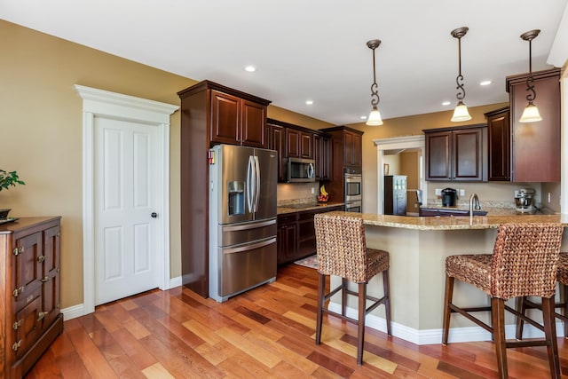 2036 Amber Wood Pl, Lancaster, OH 43130 - kitchen featuring appliances with stainless steel finishes, a peninsula, dark brown cabinets, a breakfast bar, and light wood-type flooring