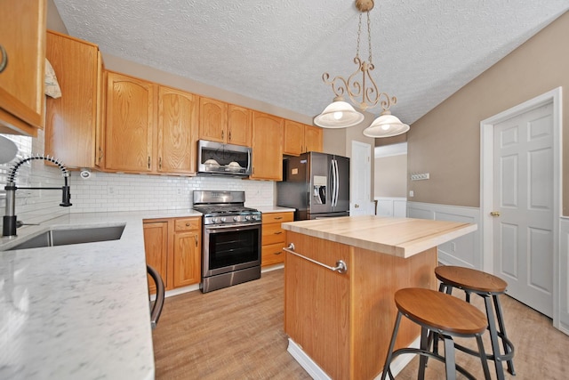 272 Trail E, Etna, OH 43062 - kitchen featuring appliances with stainless steel finishes, a sink, a kitchen island, decorative backsplash, and wainscoting