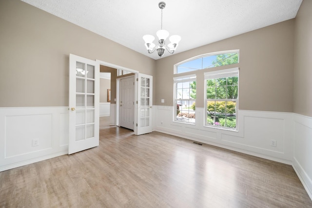 272 Trail E, Etna, OH 43062 - empty room featuring french doors, a chandelier, a wainscoted wall, a decorative wall, and light wood-style floors