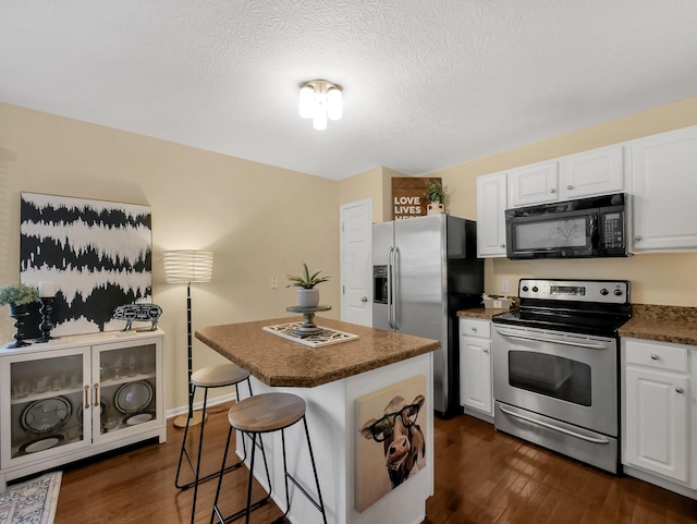 6010 Turnwood Dr Unit 703, Westerville, OH 43081 - kitchen featuring appliances with stainless steel finishes, dark wood-style flooring, white cabinets, a kitchen breakfast bar, and a textured ceiling