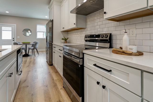 2589 Dayton Ave, Columbus, OH 43202 - kitchen with appliances with stainless steel finishes, wall chimney exhaust hood, light wood-style floors, white cabinetry, and recessed lighting