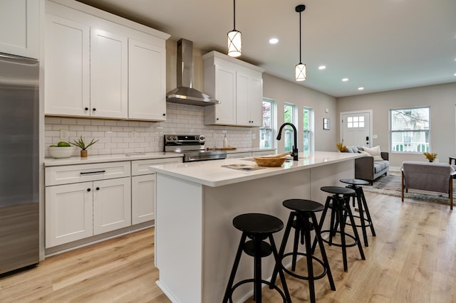 2589 Dayton Ave, Columbus, OH 43202 - kitchen with appliances with stainless steel finishes, wall chimney range hood, light wood finished floors, decorative backsplash, and a center island with sink