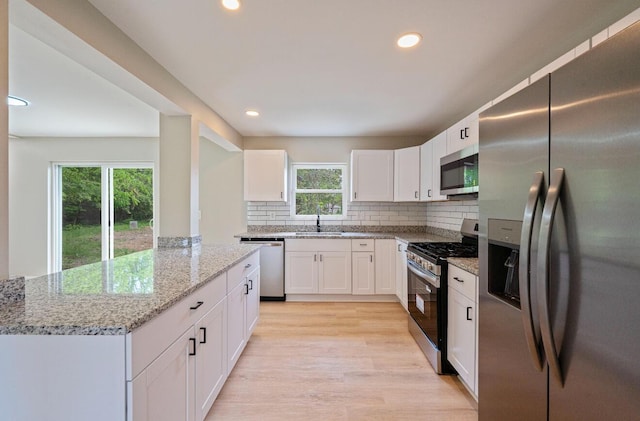 202 Toland St, London, OH 43140 - kitchen with stainless steel appliances, backsplash, light stone counters, light wood-type flooring, and white cabinetry