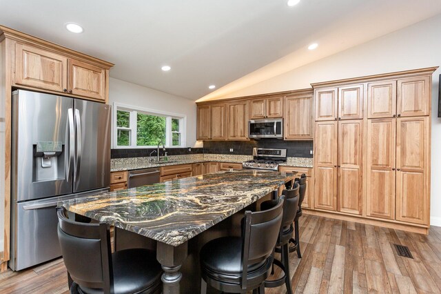 2914 Hickory Hill Dr SE, Lancaster, OH 43130 - kitchen with stainless steel appliances, vaulted ceiling, a kitchen breakfast bar, backsplash, and light wood-type flooring