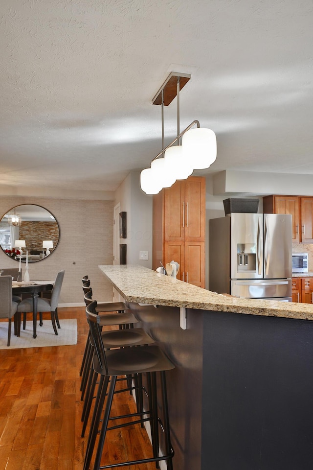 7775 Pembrook Dr, Reynoldsburg, OH 43068 - kitchen featuring stainless steel appliances, brown cabinetry, dark wood-style flooring, pendant lighting, and light stone counters