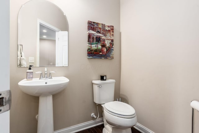 bathroom with toilet, baseboards, wood finished floors, and a sink