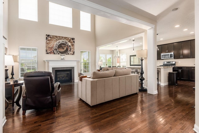 living area featuring a tiled fireplace, dark wood-type flooring, plenty of natural light, recessed lighting, and a high ceiling