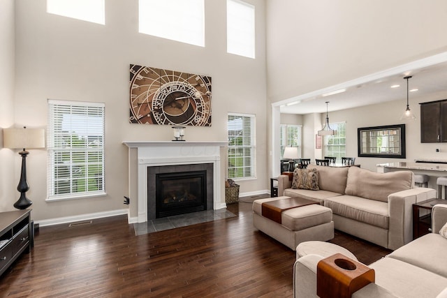 living room with dark wood-style flooring, a high ceiling, baseboards, and a tile fireplace
