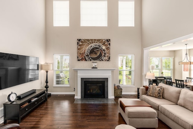 living area featuring a towering ceiling, baseboards, dark wood finished floors, and healthy amount of natural light