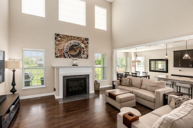 living room with a towering ceiling, dark wood finished floors, baseboards, and a tiled fireplace
