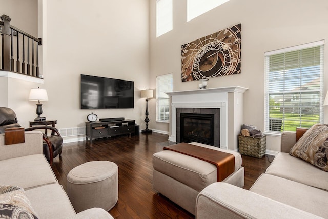 living room with a high ceiling, wood-type flooring, a tiled fireplace, and baseboards
