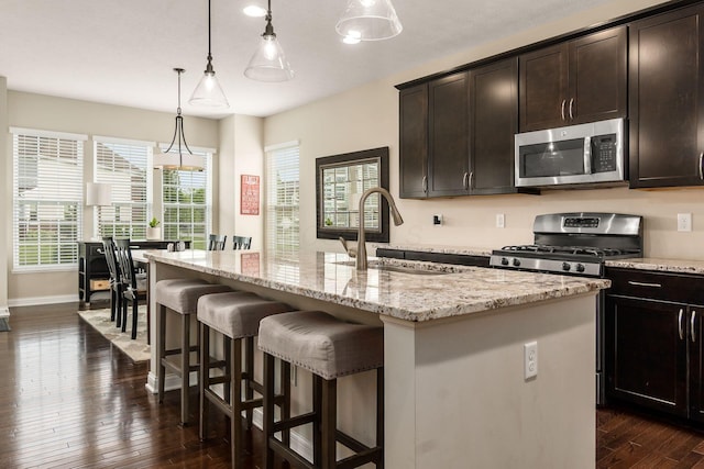 kitchen with stainless steel appliances, a sink, dark wood-style floors, light stone countertops, and pendant lighting