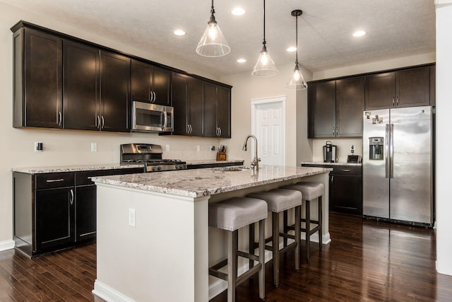 kitchen with appliances with stainless steel finishes, a sink, dark wood-type flooring, a breakfast bar area, and light stone counters