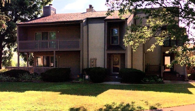 view of front facade featuring a balcony, a front lawn, and a chimney
