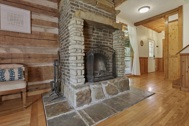 23587 Woltz Rd, Rockbridge, OH 43149 - unfurnished living room with hardwood / wood-style flooring, a wainscoted wall, a stone fireplace, beam ceiling, and wood walls