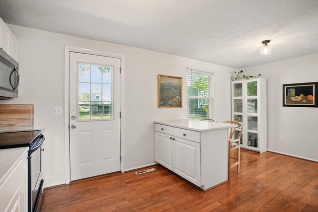 651 Dovalon Pl, Galloway, OH 43119 - kitchen featuring range with electric stovetop, stainless steel microwave, wood finished floors, a peninsula, and a textured ceiling