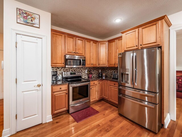 8171 Campden Lakes Blvd, Dublin, OH 43016 - kitchen featuring stainless steel appliances, light wood finished floors, tasteful backsplash, dark stone counters, and a textured ceiling