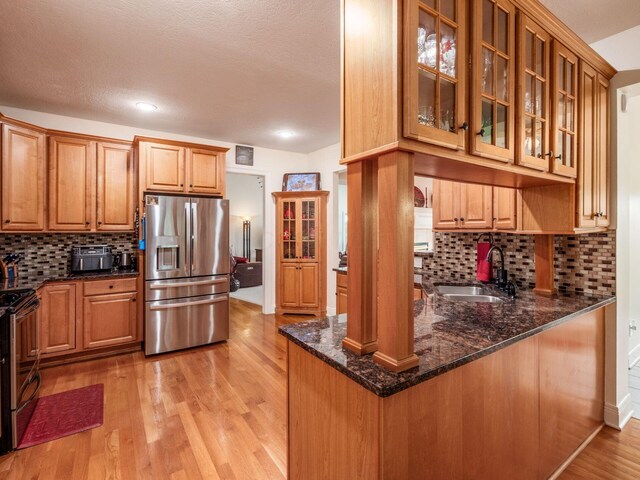 8171 Campden Lakes Blvd, Dublin, OH 43016 - kitchen featuring appliances with stainless steel finishes, a sink, light wood-style flooring, dark stone counters, and glass insert cabinets