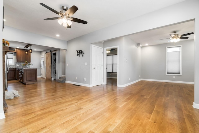 71 Market St, Carroll, OH 43112 - unfurnished living room featuring stacked washing machine and dryer, a ceiling fan, a barn door, light wood-type flooring, and healthy amount of natural light