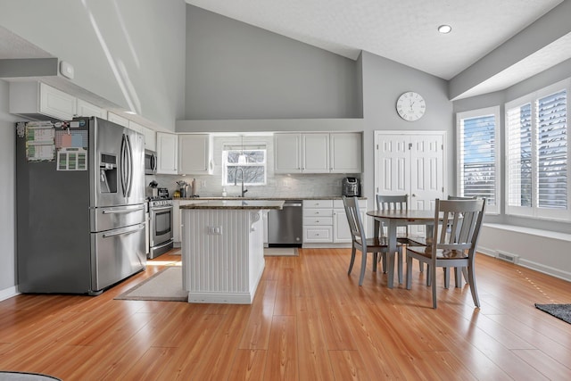 9556 Ireland Ct, Powell, OH 43065 - kitchen with stainless steel appliances, high vaulted ceiling, white cabinetry, a center island, and tasteful backsplash