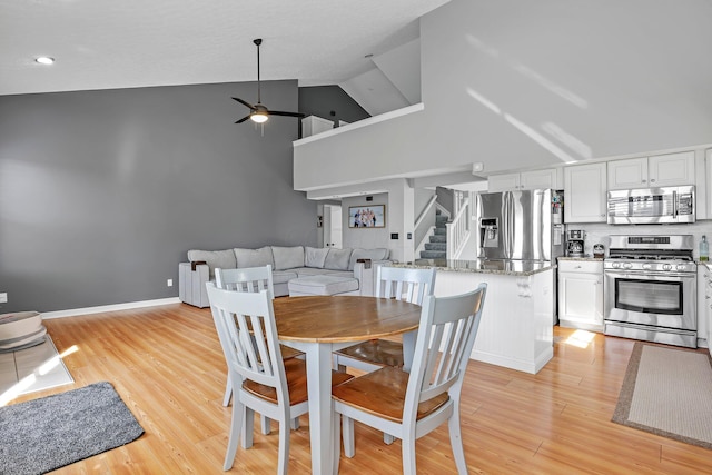 9556 Ireland Ct, Powell, OH 43065 - dining room featuring a ceiling fan, stairs, light wood-style floors, and high vaulted ceiling