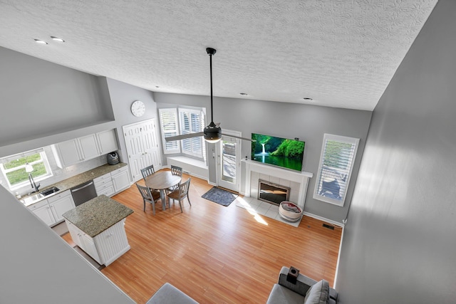 9556 Ireland Ct, Powell, OH 43065 - living room featuring ceiling fan, vaulted ceiling, a textured ceiling, a tile fireplace, and light wood-style flooring