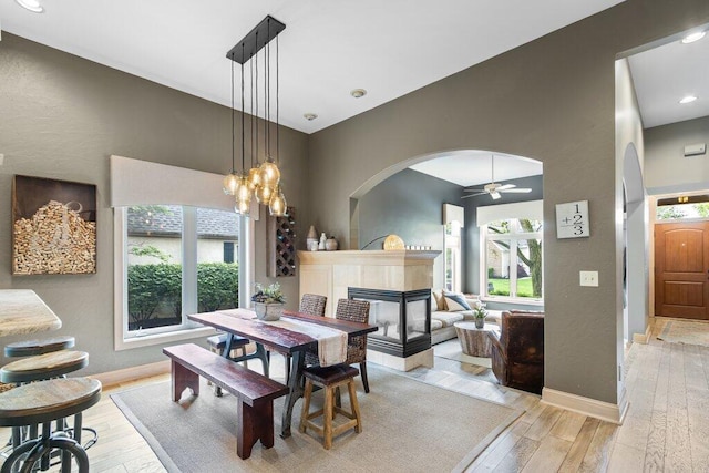 4367 Tavistock Cir, Powell, OH 43065 - dining space featuring light wood-style flooring, arched walkways, ceiling fan, baseboards, and a fireplace