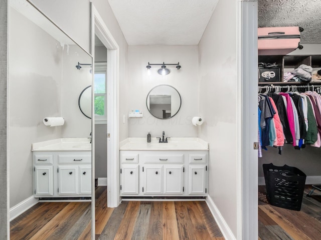 7121 Briarcliff Rd, Reynoldsburg, OH 43068 - bathroom with two vanities, wood finished floors, a walk in closet, a textured ceiling, and baseboards