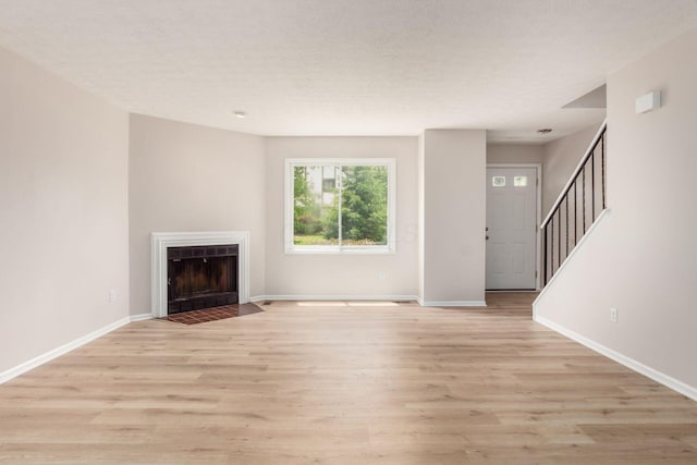 2353 Mccauley Ct Unit 6, Columbus, OH 43220 - unfurnished living room with baseboards, a fireplace with flush hearth, light wood-style flooring, stairs, and a textured ceiling