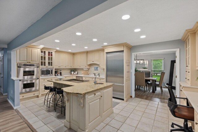 5210 Chevy Chase Ct, Columbus, OH 43220 - kitchen with built in appliances, a center island with sink, a breakfast bar area, a sink, and decorative backsplash