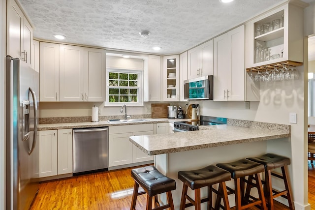 590 Haversham Dr, Gahanna, OH 43230 - kitchen featuring stainless steel appliances, a peninsula, a kitchen bar, glass insert cabinets, and a textured ceiling