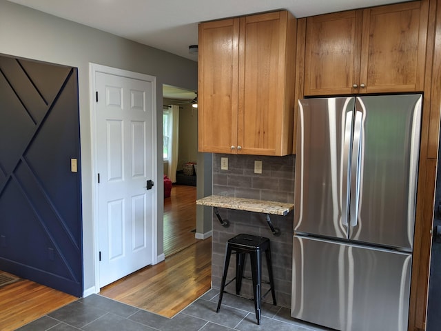 198 Loveman Ave, Worthington, OH 43085 - kitchen with freestanding refrigerator, dark tile patterned flooring, brown cabinetry, decorative backsplash, and a breakfast bar area