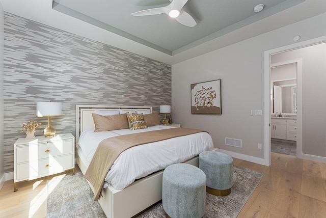 8159 Riverside Dr, Powell, OH 43065 - bedroom featuring wood finished floors, an accent wall, a tray ceiling, baseboards, and wallpapered walls